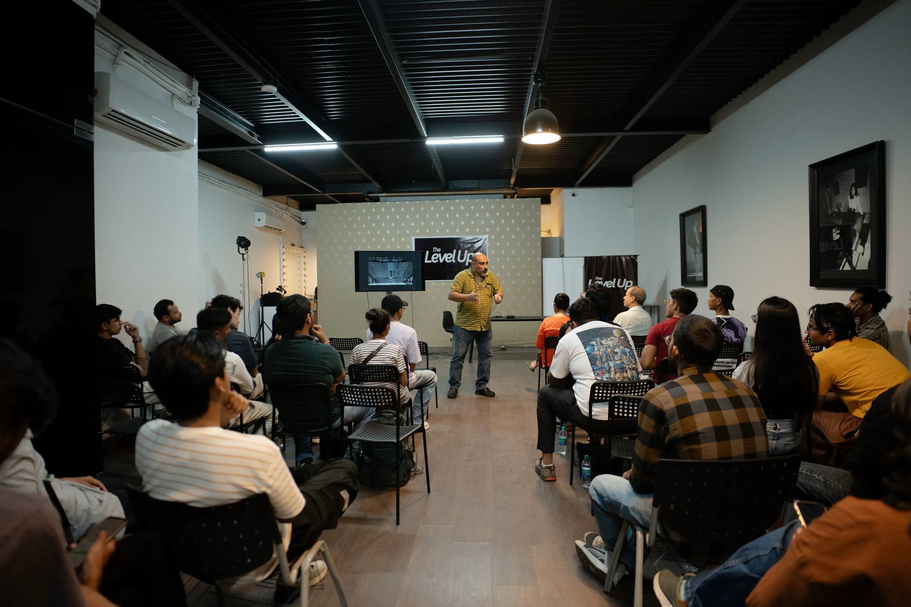 A facilitator leading a workshop in a wide room, with the seated participants seen from behind